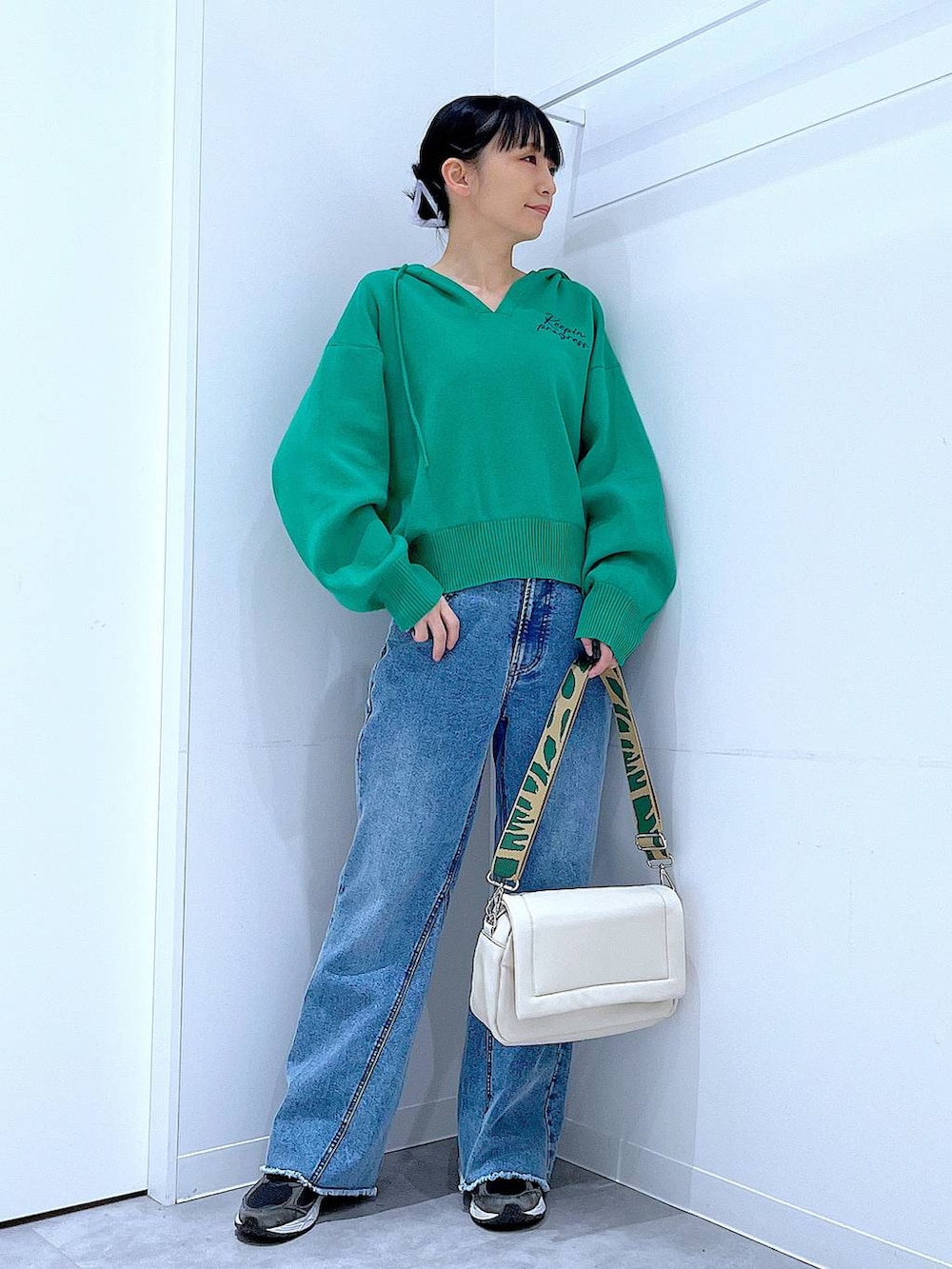 ホワイト系のショルダーバッグ、グリーン系のニット/セーター、ブルー系のデニムパンツを着用したレディースの春コーディネートの2枚目の写真