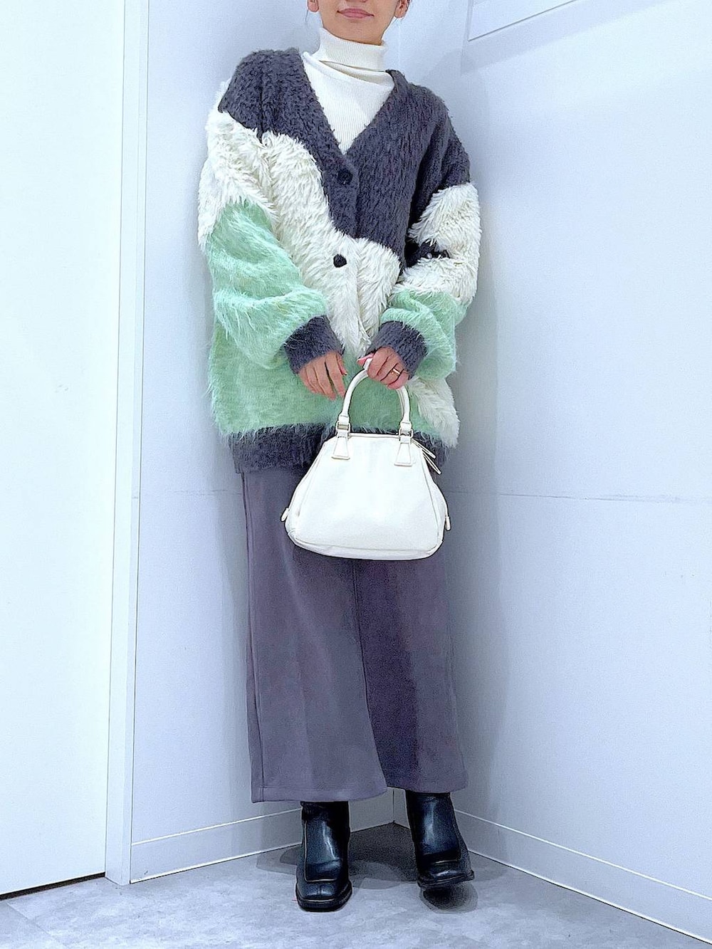 グリーン系のカーディガン/ボレロ、ブラック系のブーツ、ホワイト系のショルダーバッグを着用したレディースの冬コーディネートの6枚目の写真