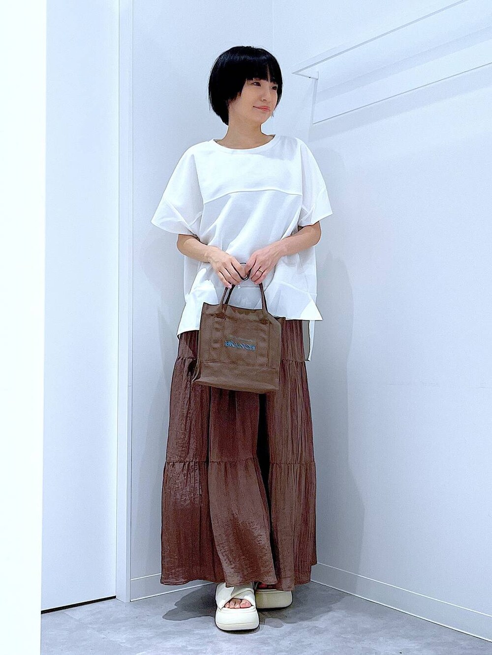 ホワイト系のサンダル、ホワイト系のTシャツ/カットソー、ブラウン系のスカートを着用したレディースの夏コーディネートの2枚目の写真
