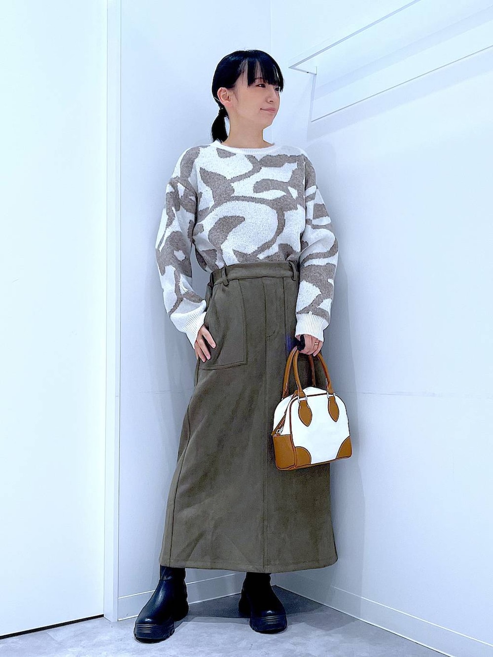ブラック系のブーツ、ホワイト系のハンドバッグ、グリーン系のスカートを着用したレディースの秋コーディネートの2枚目の写真