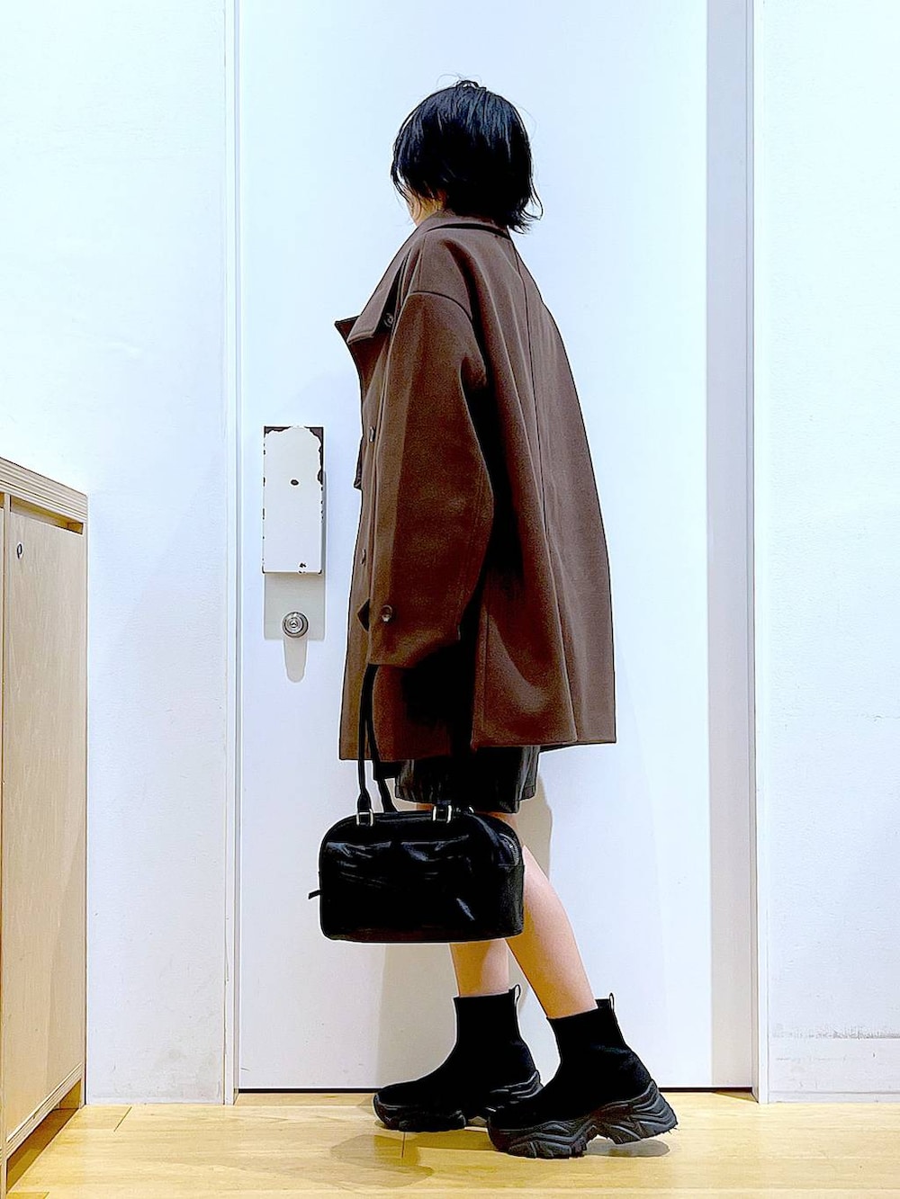 ブラウン系のステンカラーコート、ブラック系のハンドバッグ、ブラック系のブーツを着用したレディースの冬コーディネートの3枚目の写真