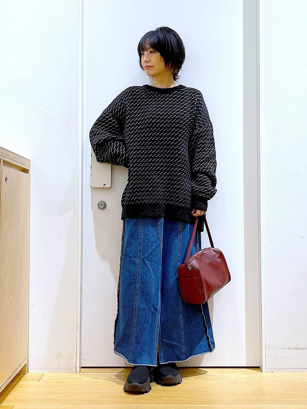 レッド系のショルダーバッグ、ブルー系のデニムスカート、ブラック系のニット/セーターを着用したレディースの冬コーディネートの2枚目の写真