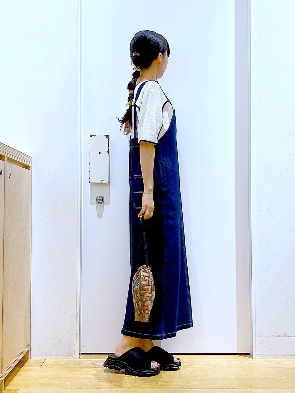 ブルー系のジャンパースカート、ブラウン系のショルダーバッグ、ブラック系のサンダルを着用したレディースの夏コーディネートの4枚目の写真