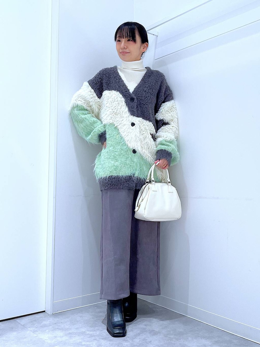 グリーン系のカーディガン/ボレロ、ブラック系のブーツ、ホワイト系のショルダーバッグを着用したレディースの冬コーディネートの2枚目の写真