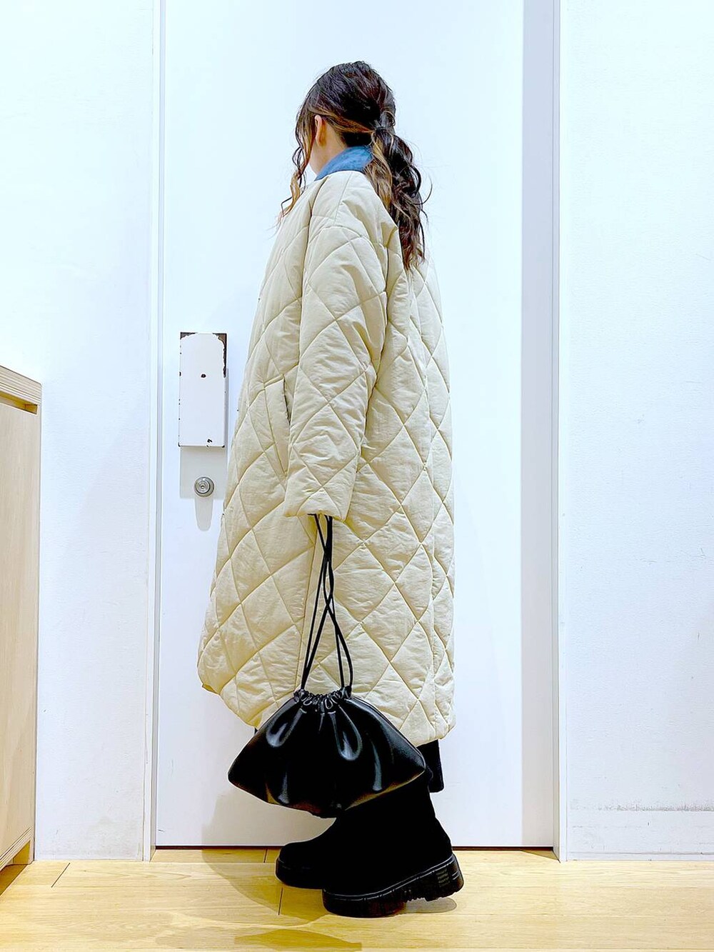 ブラック系のショルダーバッグ、ブラック系のブーツ、ベージュ系のノーカラーコートを着用したレディースの冬コーディネートの3枚目の写真