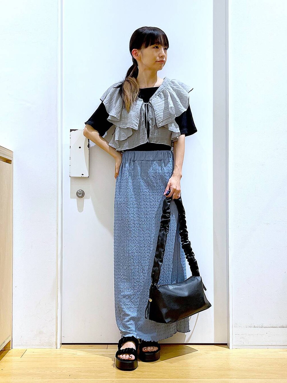 ブラック系のショルダーバッグ、ブルー系のスカート、ブラック系のTシャツ/カットソーを着用したレディースの夏コーディネートの2枚目の写真