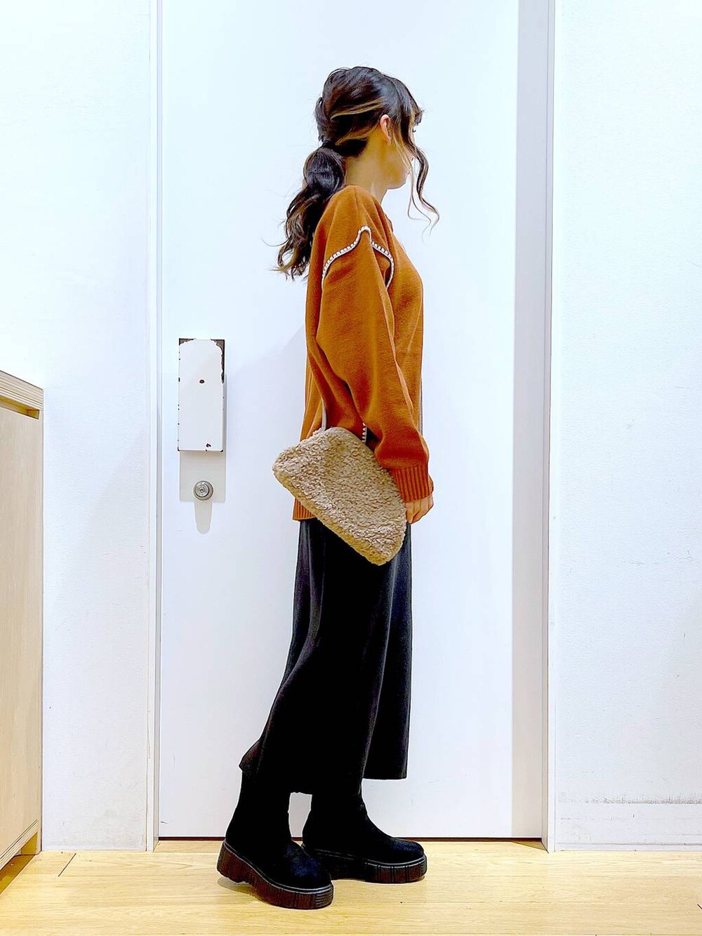 グレー系のスカート、オレンジ系のニット/セーター、ブラウン系のクラッチバッグを着用したレディースの冬コーディネートの4枚目の写真