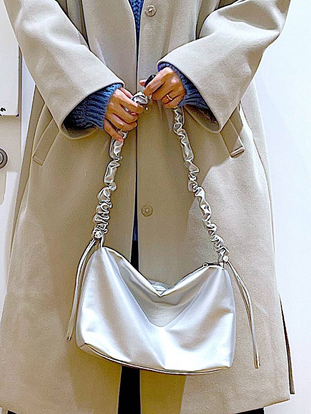 シルバー系のショルダーバッグ、ベージュ系のスニーカー、ベージュ系のノーカラーコートを着用したレディースの冬コーディネートの9枚目の写真