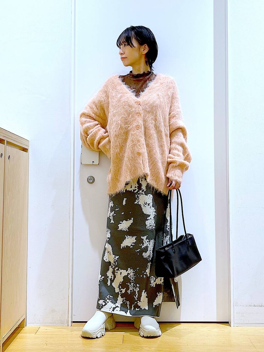 グレー系のスカート、ブラック系のトートバッグ、ピンク系のカーディガン/ボレロを着用したレディースの秋コーディネートの2枚目の写真