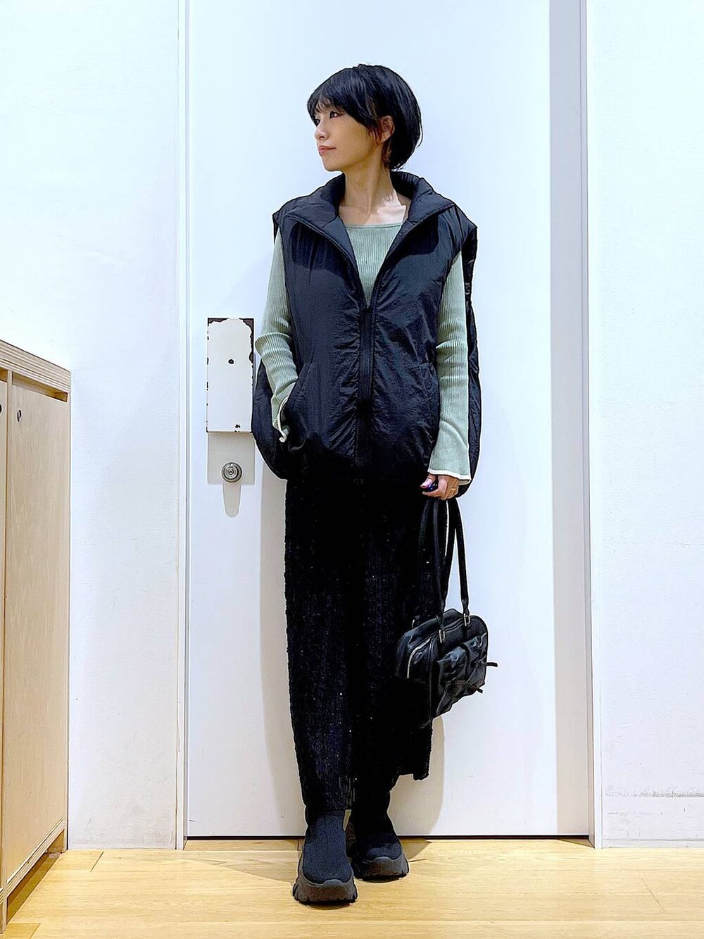 グリーン系のニット/セーター、ブラック系のハンドバッグ、ブラック系のブーツを着用したレディースの秋コーディネートの2枚目の写真