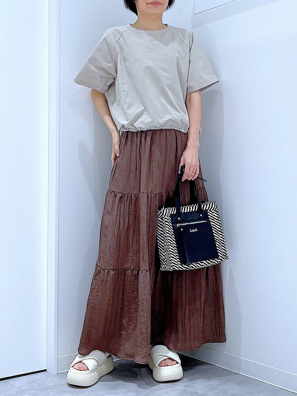 ブラック系のショルダーバッグ、ホワイト系のサンダル、ベージュ系のTシャツ/カットソーを着用したレディースの夏コーディネートの6枚目の写真