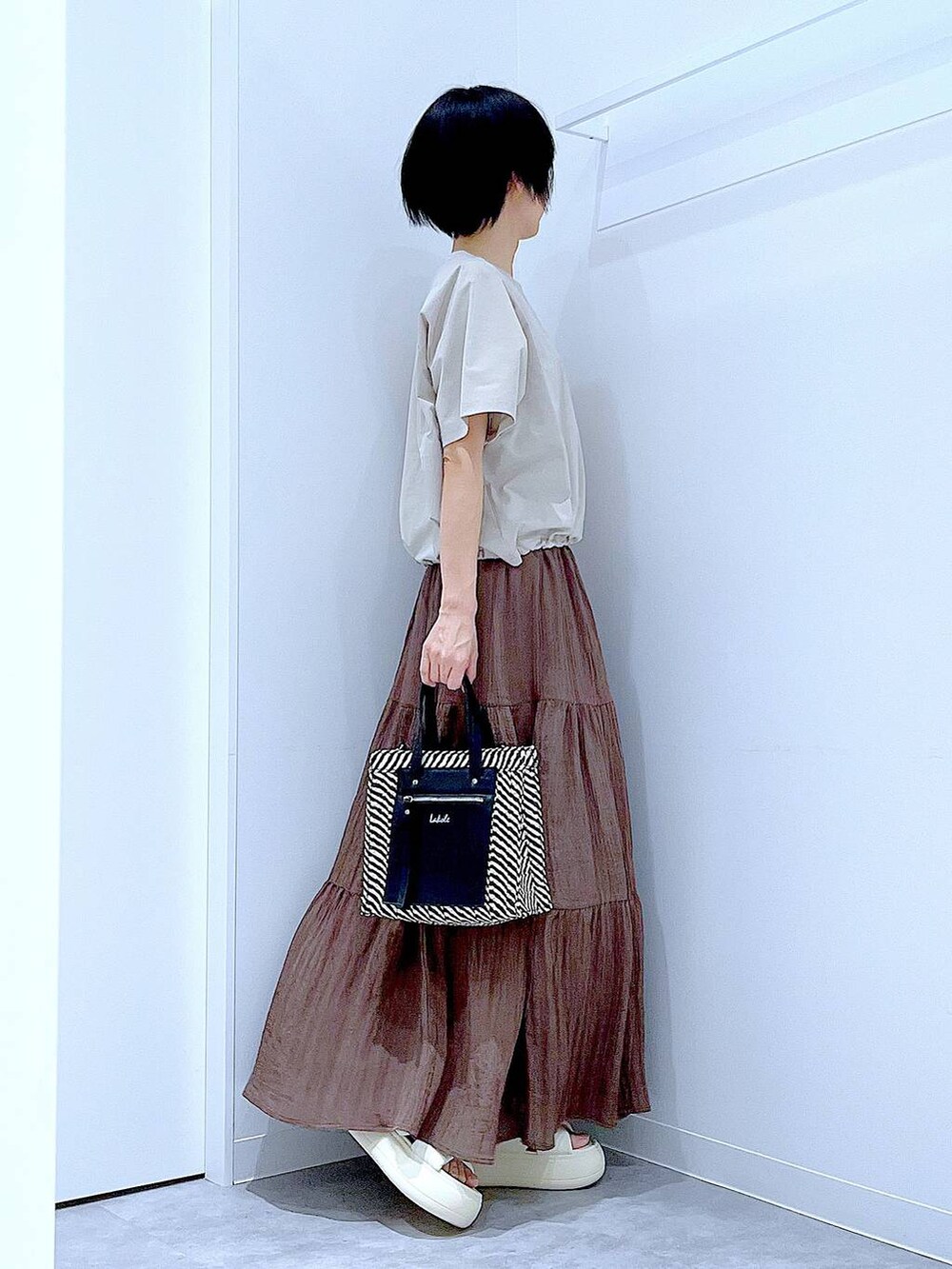 ブラック系のショルダーバッグ、ホワイト系のサンダル、ベージュ系のTシャツ/カットソーを着用したレディースの夏コーディネートの4枚目の写真