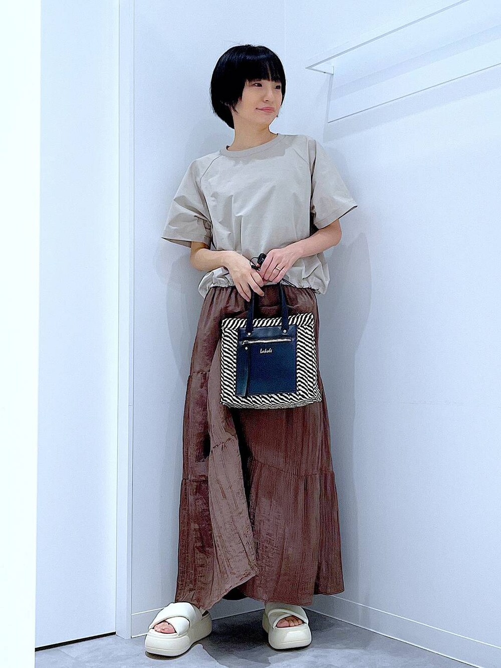 ブラック系のショルダーバッグ、ホワイト系のサンダル、ベージュ系のTシャツ/カットソーを着用したレディースの夏コーディネートの2枚目の写真