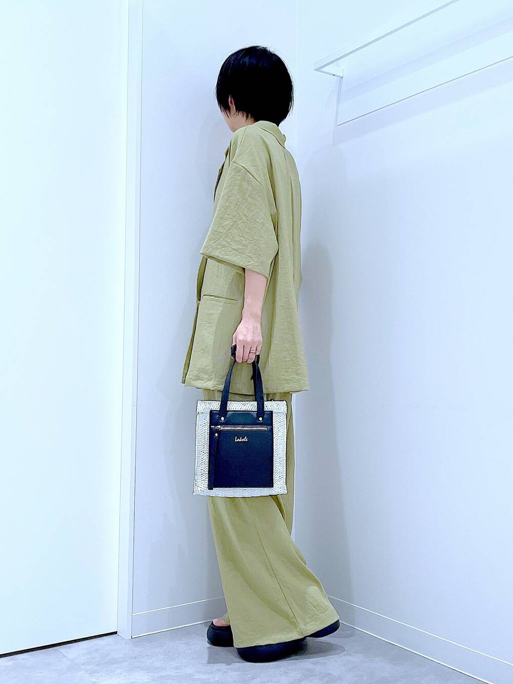 ホワイト系のショルダーバッグ、ブラック系のサンダル、グリーン系のテーラードジャケットを着用したレディースの夏コーディネートの3枚目の写真