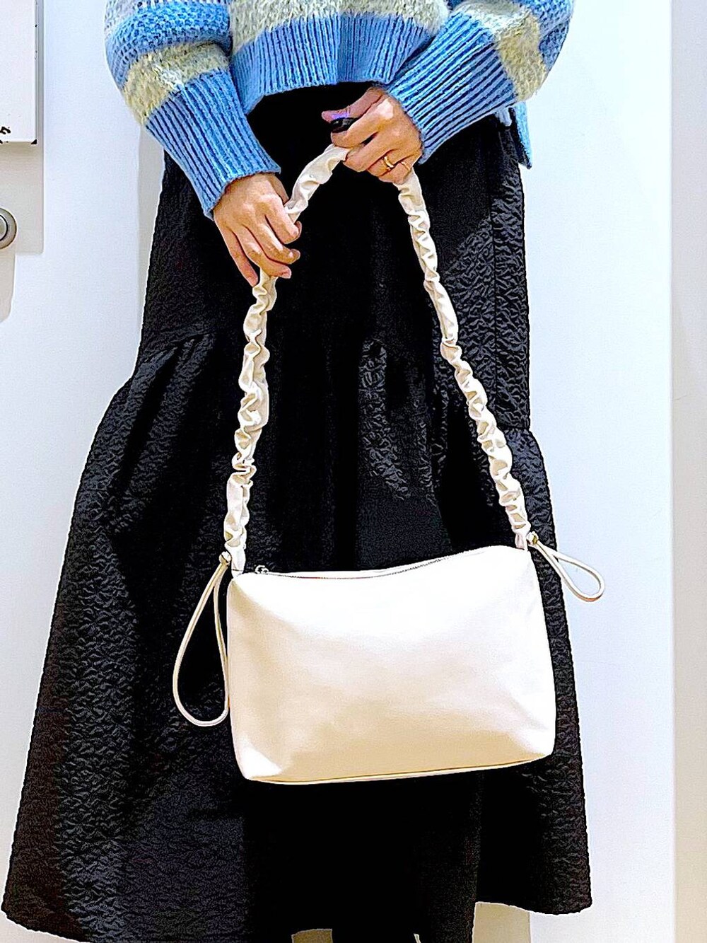 ホワイト系のショルダーバッグ、ブラック系のブーツ、ブラック系のスカートを着用したレディースの冬コーディネートの9枚目の写真