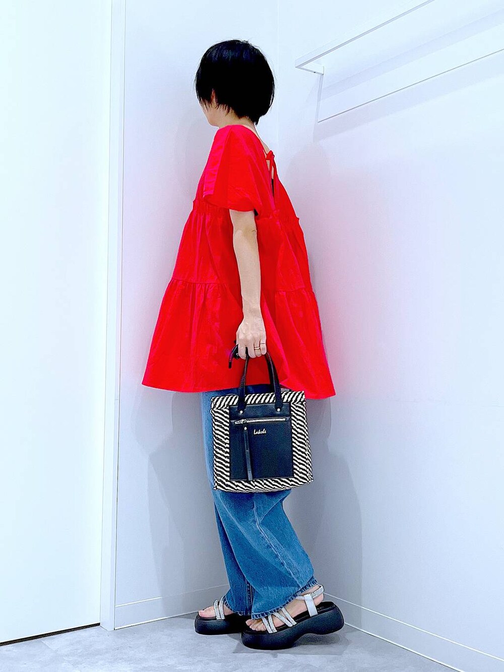 ブルー系のデニムパンツ、ブラック系のショルダーバッグ、シルバー系のサンダルを着用したレディースの夏コーディネートの3枚目の写真