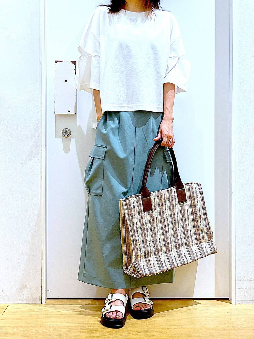 ホワイト系のサンダル、グリーン系のスカート、ブラウン系のトートバッグを着用したレディースの夏コーディネートの6枚目の写真