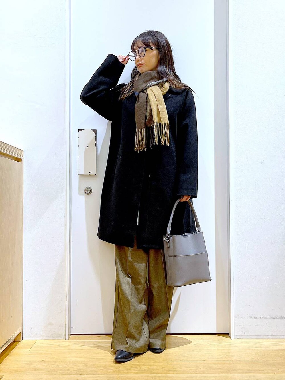 ブラック系のノーカラーコート、グレー系のショルダーバッグ、グレー系のニット/セーターを着用したレディースの冬コーディネートの2枚目の写真