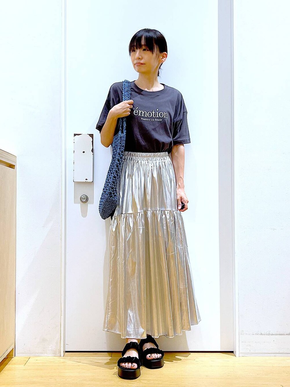 ブラック系のサンダル、シルバー系のスカート、ブルー系のトートバッグを着用したレディースの夏コーディネートの2枚目の写真