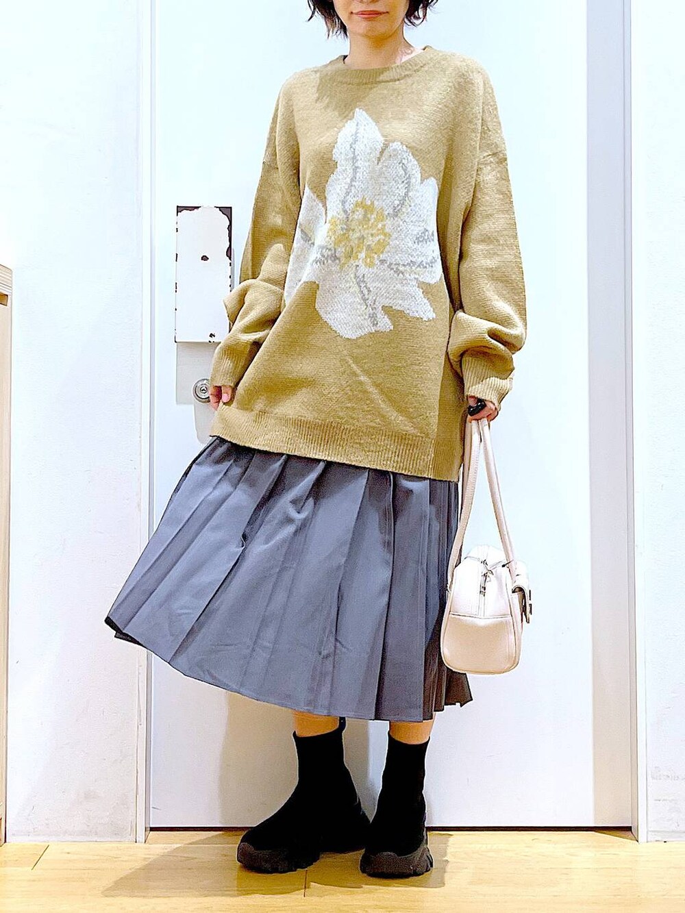 ホワイト系のハンドバッグ、ブラック系のブーツ、グレー系のスカートを着用したレディースの冬コーディネートの6枚目の写真