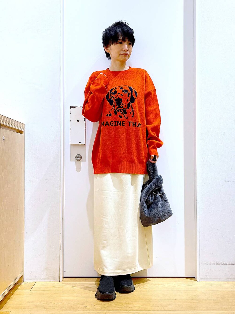 グレー系のショルダーバッグ、オレンジ系のニット/セーター、ブラック系のブーツを着用したレディースの冬コーディネートの2枚目の写真