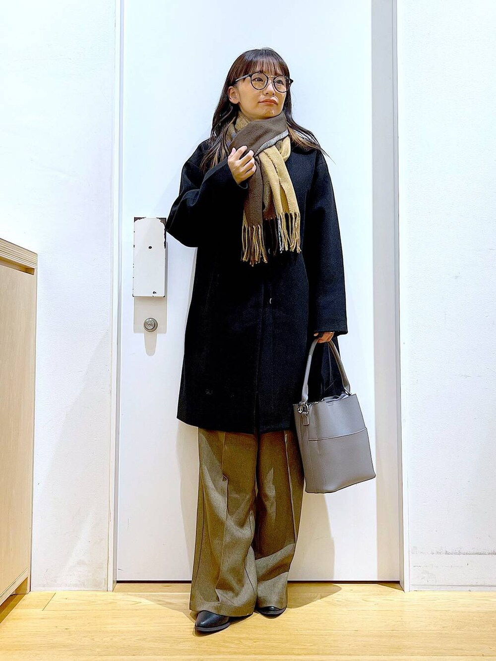 ブラック系のノーカラーコート、グレー系のショルダーバッグ、グレー系のニット/セーターを着用したレディースの冬コーディネートの3枚目の写真