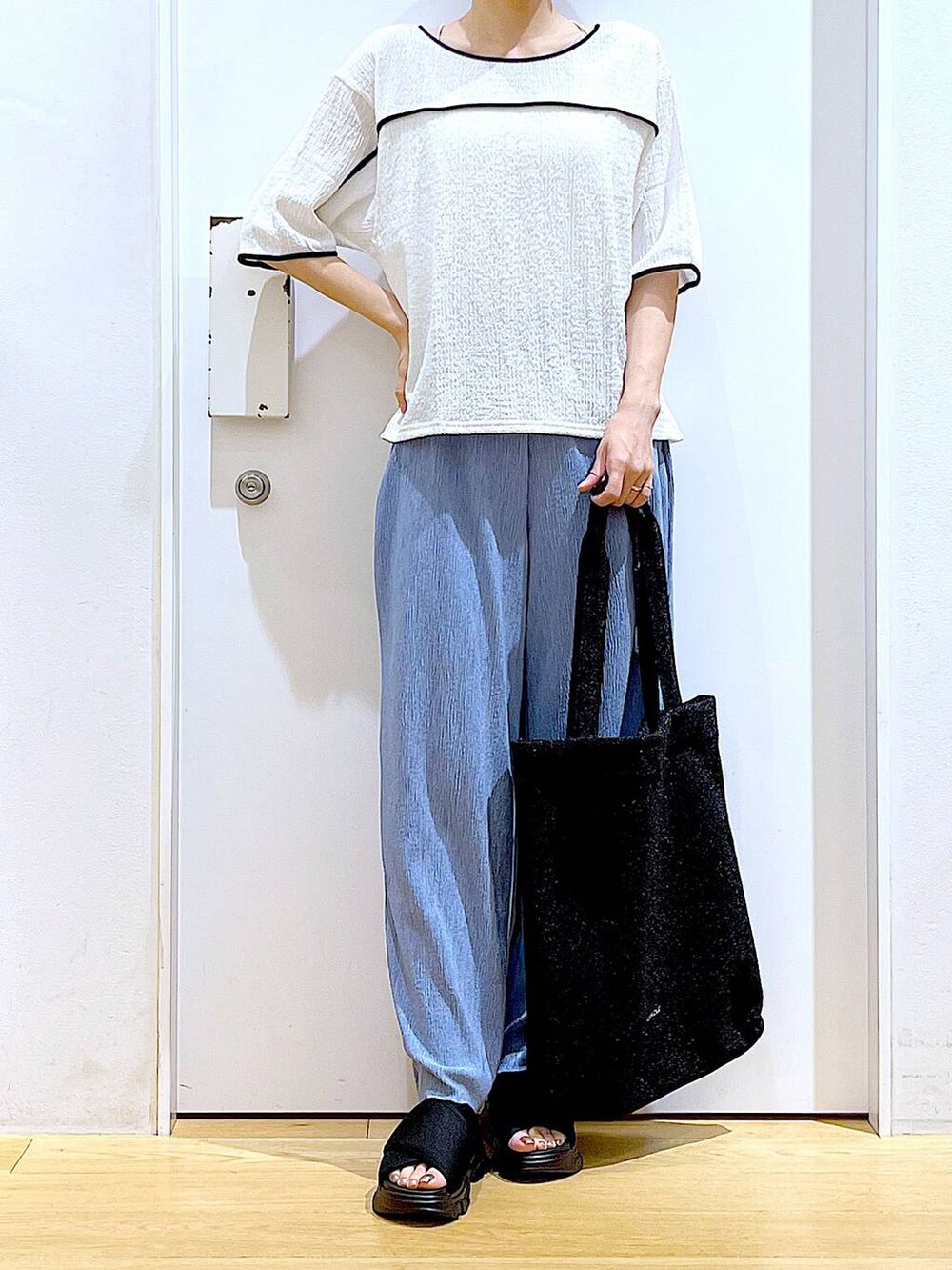 ブラック系のトートバッグ、ブラック系のサンダル、ホワイト系のTシャツ/カットソーを着用したレディースの夏コーディネートの6枚目の写真