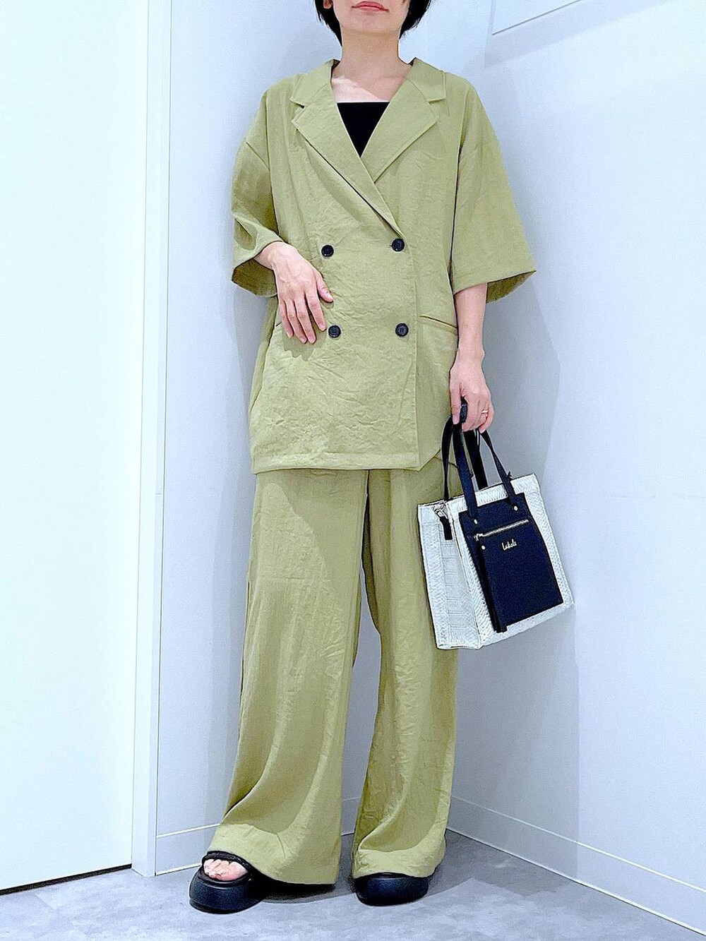 ホワイト系のショルダーバッグ、ブラック系のサンダル、グリーン系のテーラードジャケットを着用したレディースの夏コーディネートの6枚目の写真