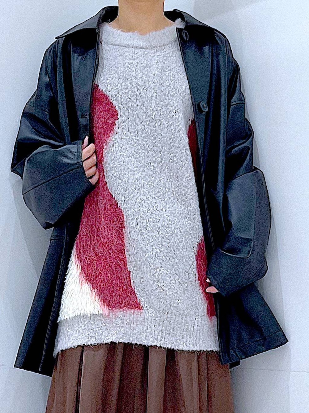 ブラック系のステンカラーコート、レッド系のニット/セーター、ブラック系のブーツを着用したレディースの冬コーディネートの7枚目の写真