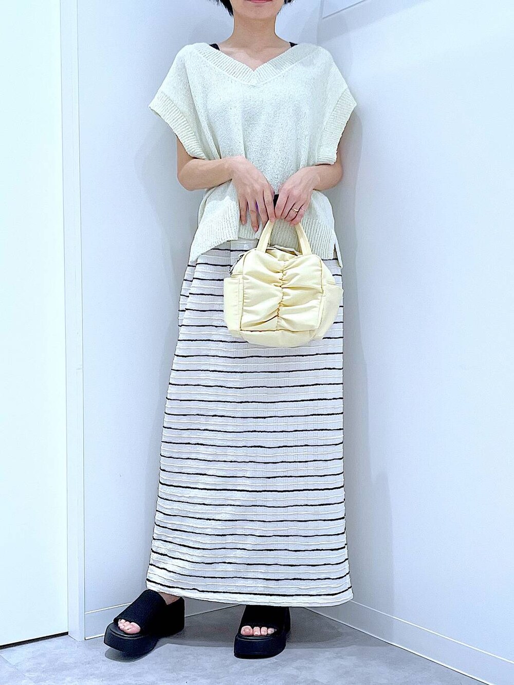 ブラック系のサンダル、イエロー系のショルダーバッグ、ホワイト系のスカートを着用したレディースの夏コーディネートの6枚目の写真