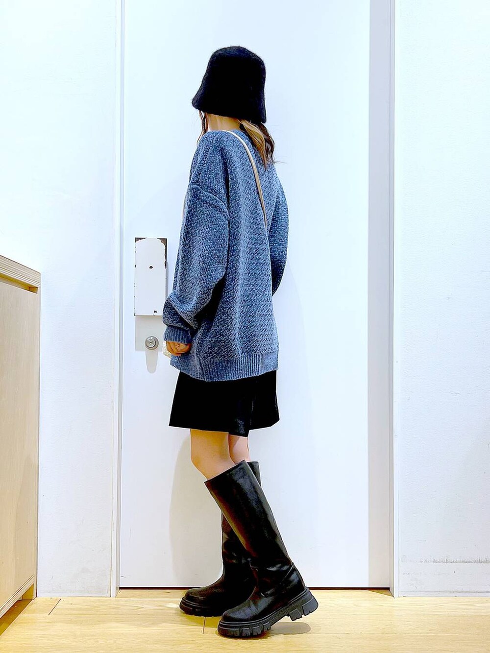 ブルー系のニット/セーター、ホワイト系のクラッチバッグ、ブラック系のブーツを着用したレディースの冬コーディネートの3枚目の写真