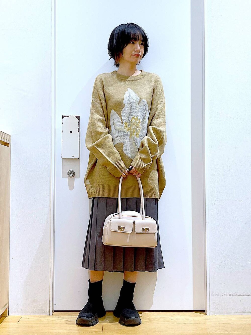 ホワイト系のハンドバッグ、ブラック系のブーツ、グレー系のスカートを着用したレディースの冬コーディネートの2枚目の写真