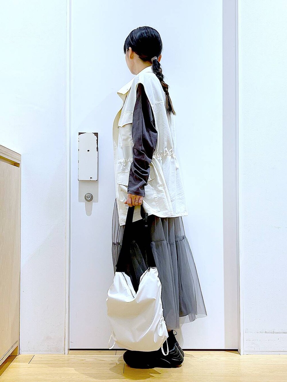 グレー系のスカート、ブラック系のスニーカー、ホワイト系のベストを着用したレディースの春コーディネートの3枚目の写真