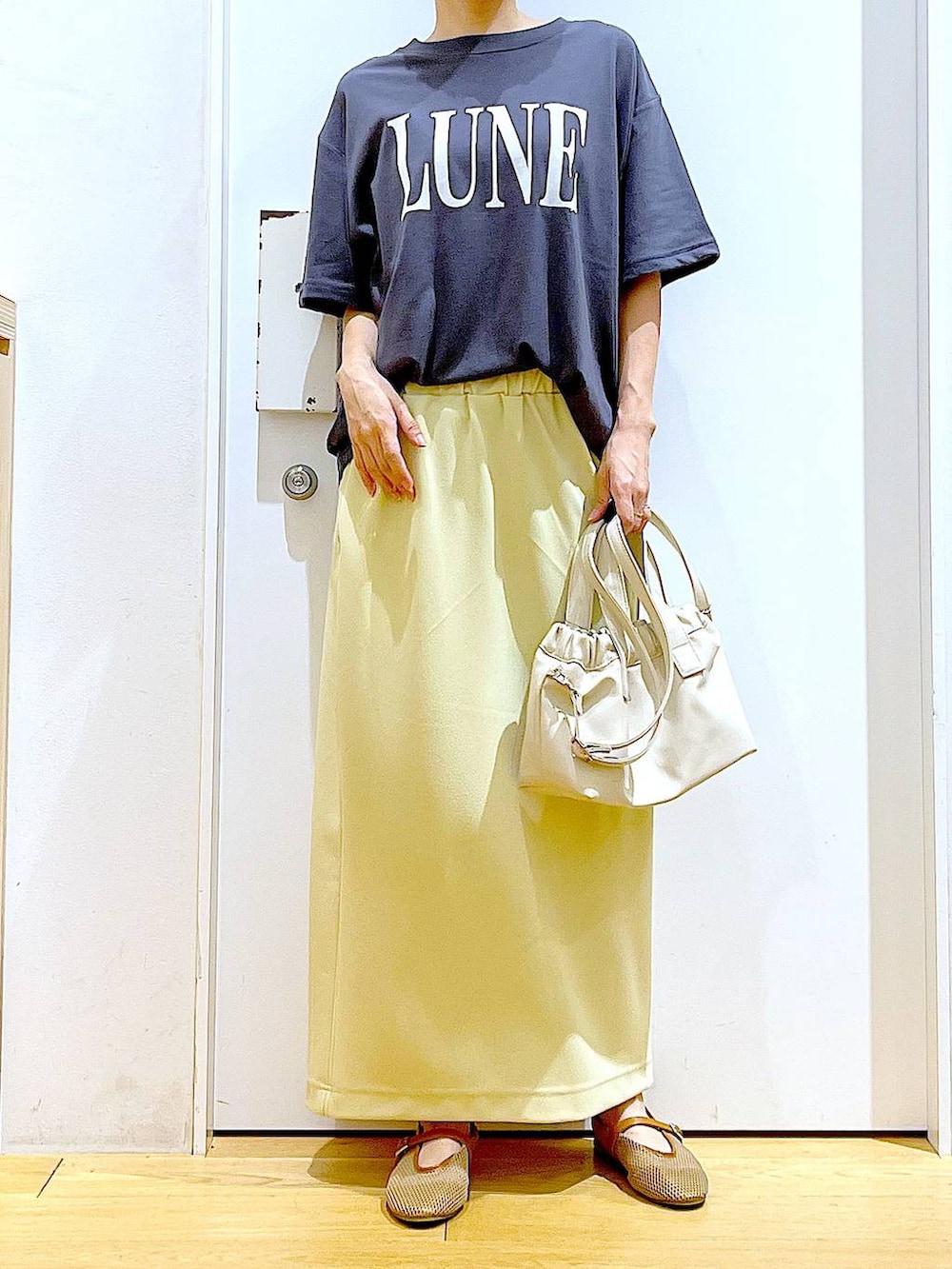 ホワイト系のショルダーバッグ、ベージュ系のパンプス、イエロー系のスカートを着用したレディースの夏コーディネートの6枚目の写真