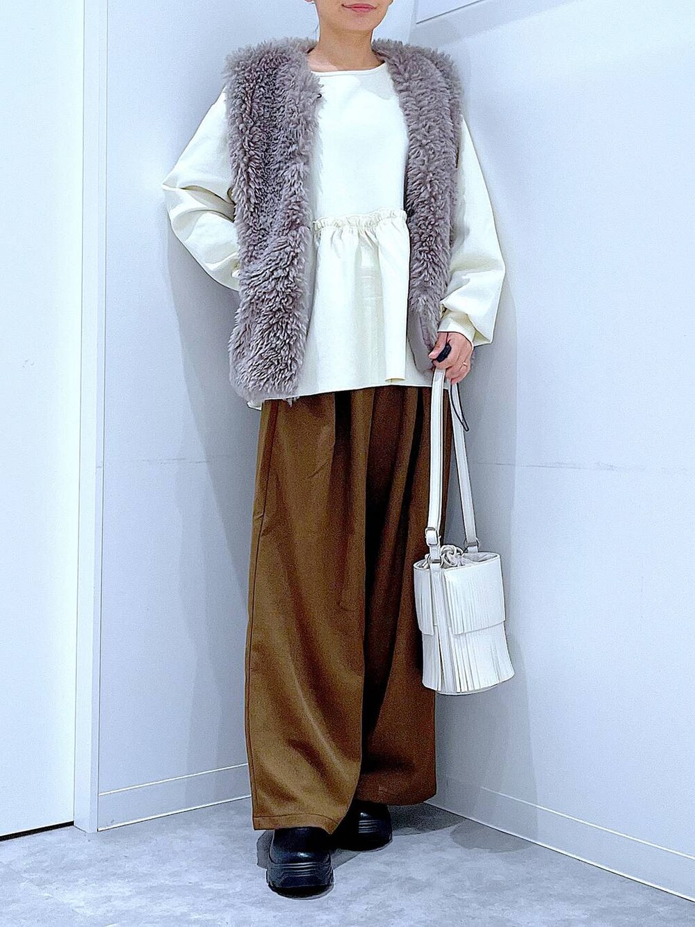 グレー系のベスト、ホワイト系のショルダーバッグ、ブラック系のブーツを着用したレディースの冬コーディネートの6枚目の写真