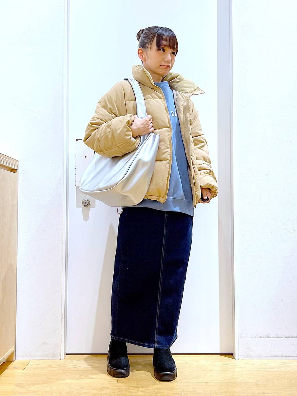 シルバー系のトートバッグ、ベージュ系のナイロンジャケット、ブルー系のデニムスカートを着用したレディースの冬コーディネートの2枚目の写真
