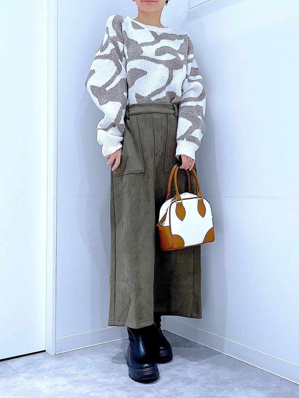 ブラック系のブーツ、ホワイト系のハンドバッグ、グリーン系のスカートを着用したレディースの秋コーディネートの6枚目の写真