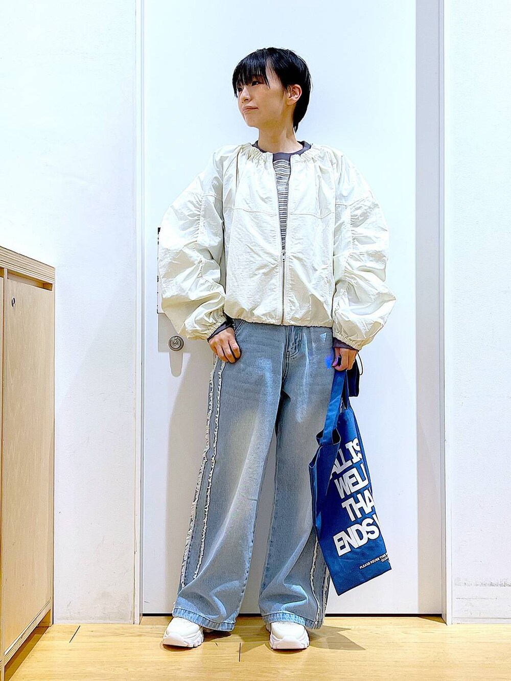 ホワイト系のスニーカー、ブルー系のデニムパンツ、ホワイト系のブルゾンを着用したレディースの春コーディネートの2枚目の写真