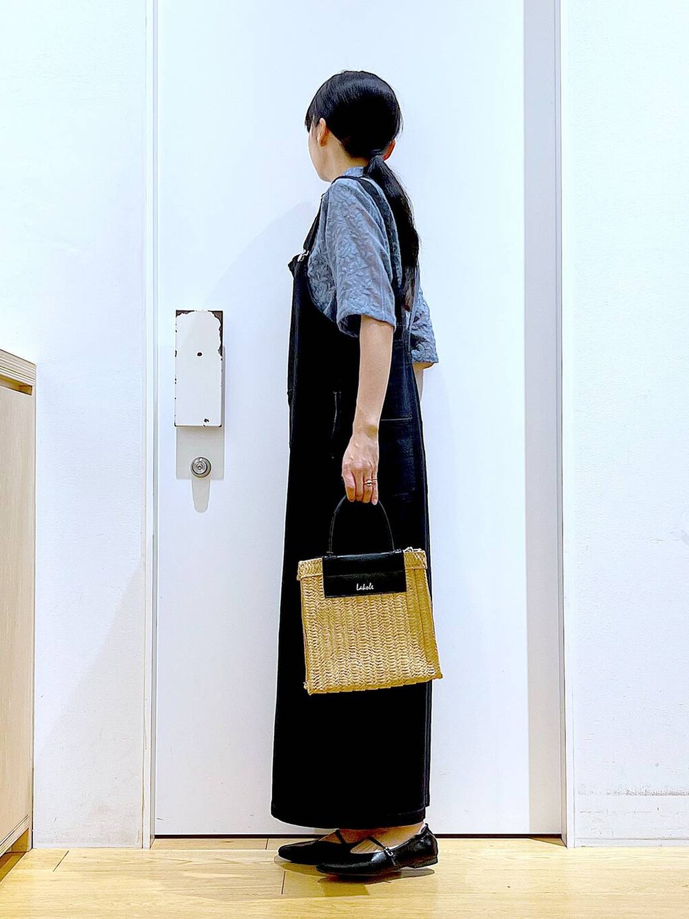 グレー系のジャンパースカート、ブラック系のパンプス、ベージュ系のショルダーバッグを着用したレディースの夏コーディネートの3枚目の写真