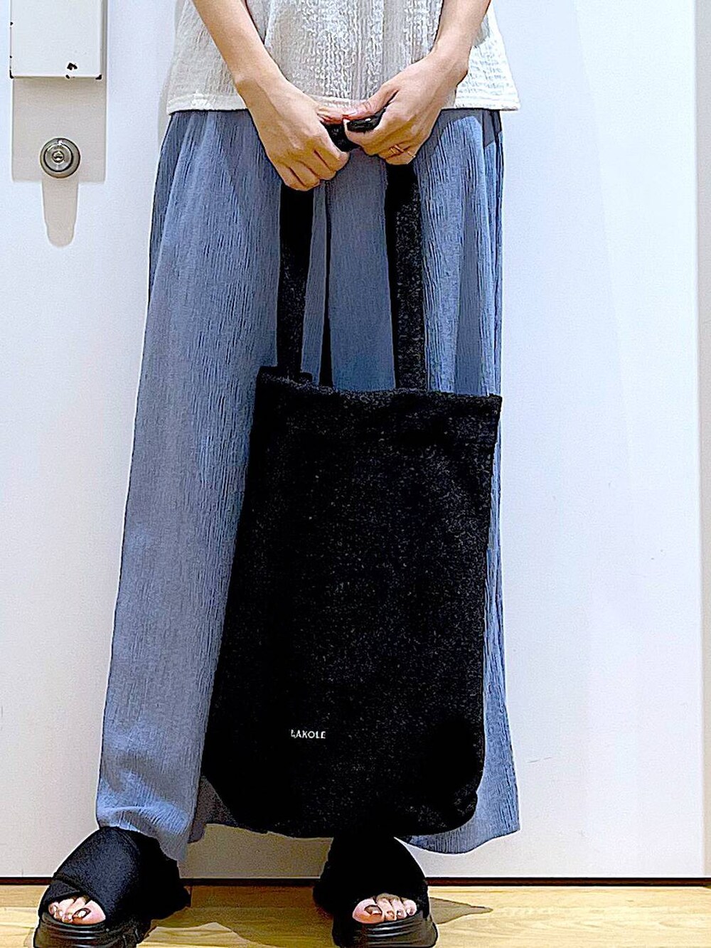 ブラック系のトートバッグ、ブラック系のサンダル、ホワイト系のTシャツ/カットソーを着用したレディースの夏コーディネートの9枚目の写真