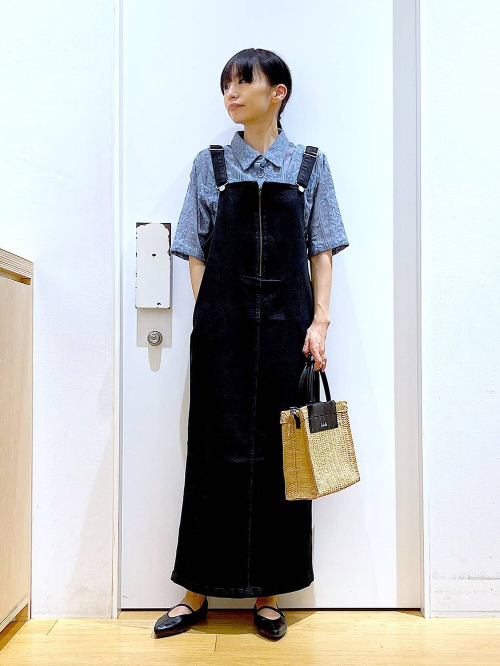 グレー系のジャンパースカート、ブラック系のパンプス、ベージュ系のショルダーバッグを着用したレディースの夏コーディネートの2枚目の写真
