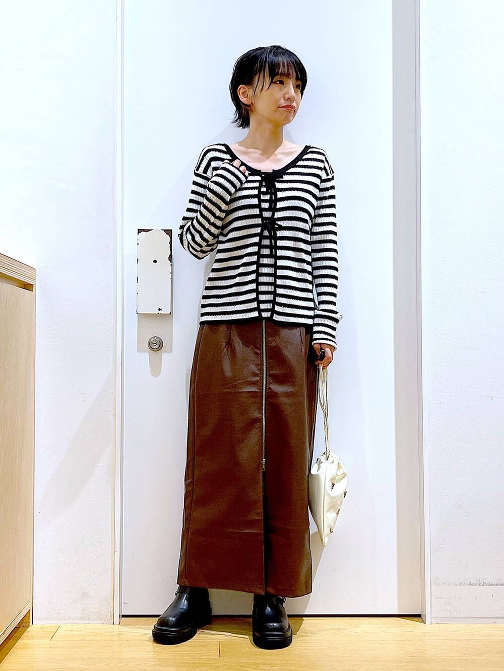 ブラウン系のスカート、ホワイト系のショルダーバッグ、ブラック系のブーツを着用したレディースの秋コーディネートの2枚目の写真