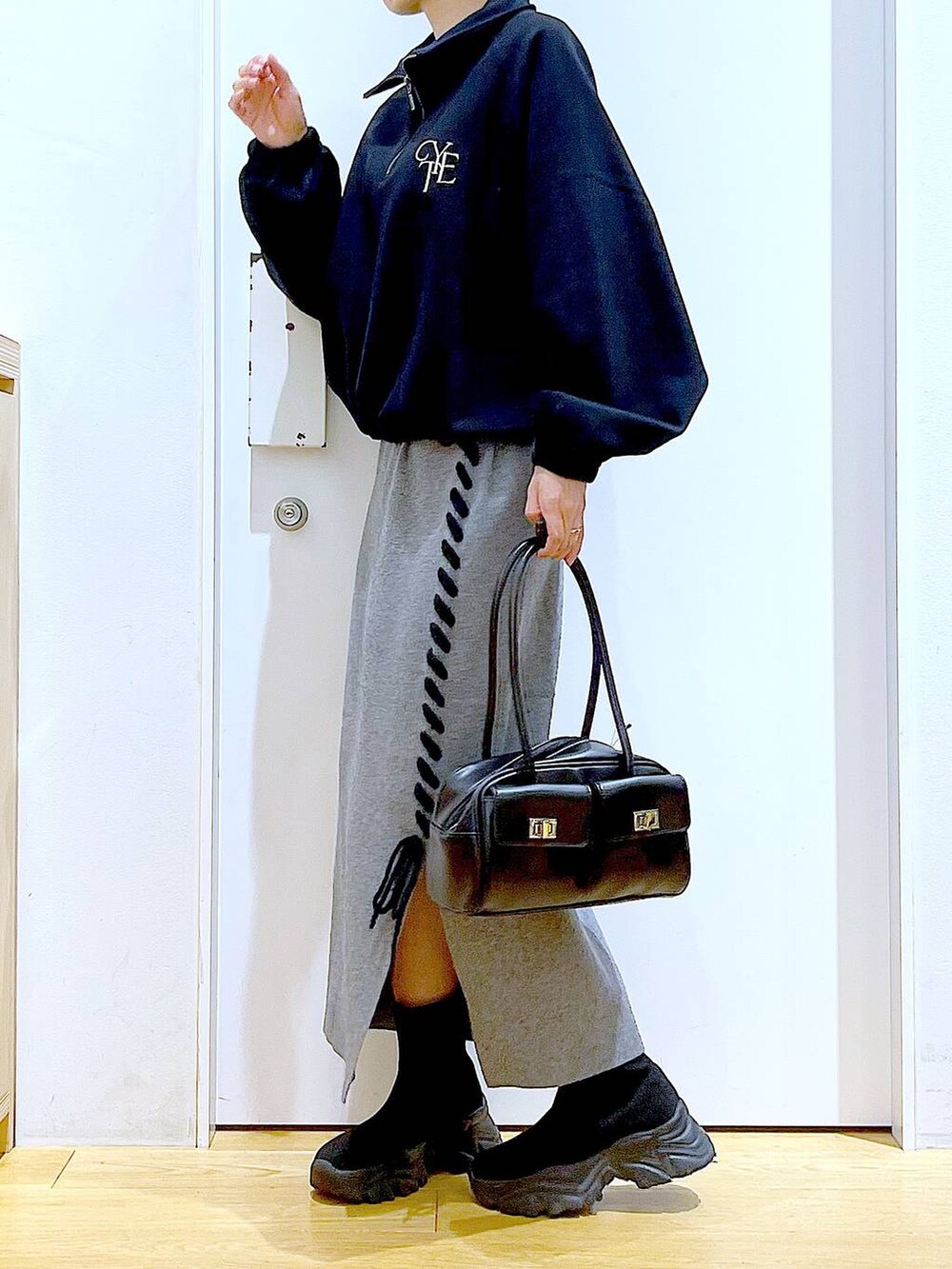 ブラック系のハンドバッグ、ブラック系のブーツ、グレー系のスカートを着用したレディースの冬コーディネートの3枚目の写真