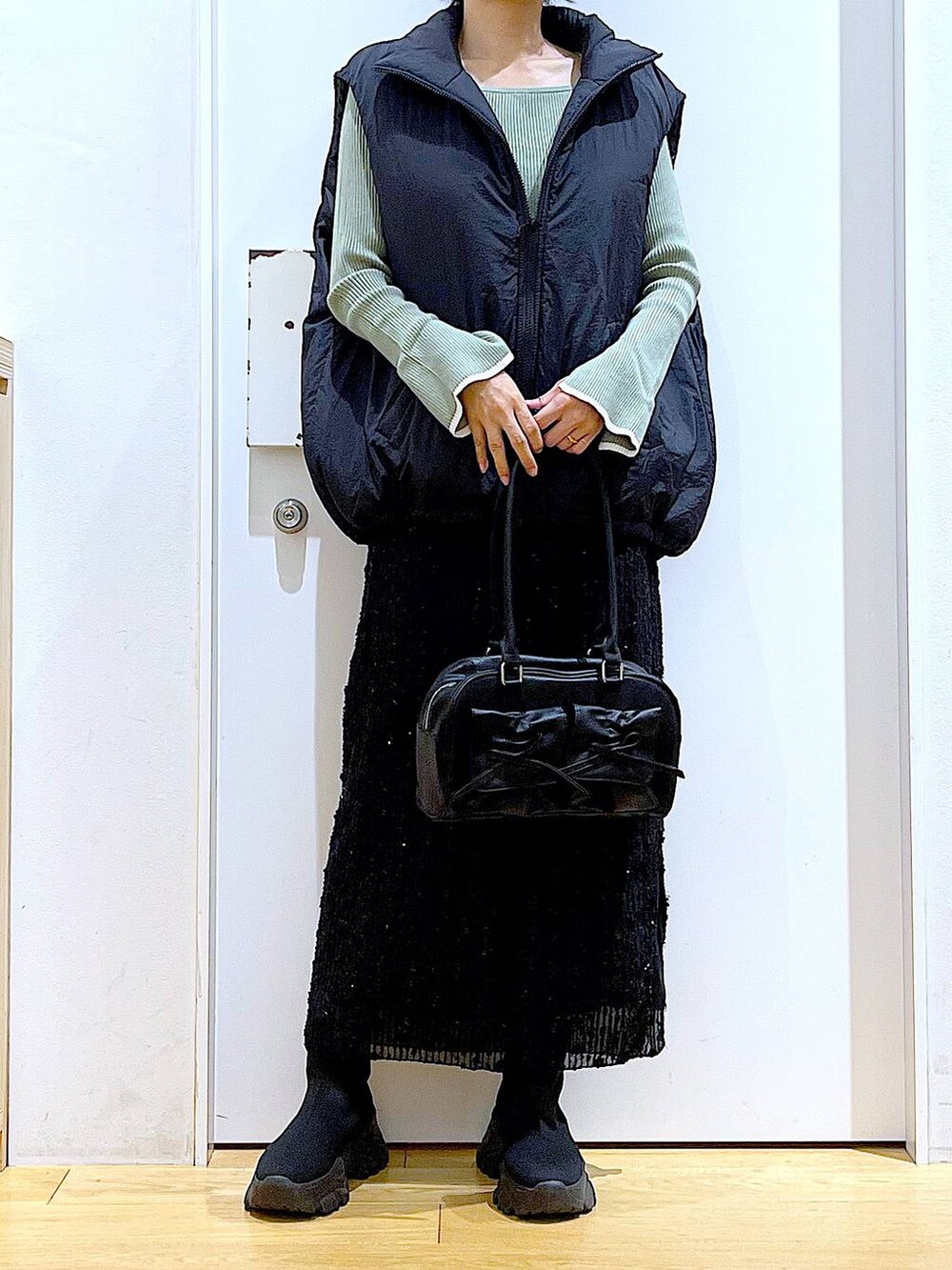 グリーン系のニット/セーター、ブラック系のハンドバッグ、ブラック系のブーツを着用したレディースの秋コーディネートの6枚目の写真