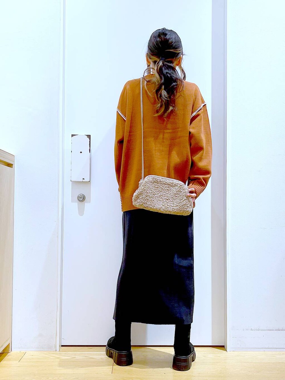 グレー系のスカート、オレンジ系のニット/セーター、ブラウン系のクラッチバッグを着用したレディースの冬コーディネートの5枚目の写真