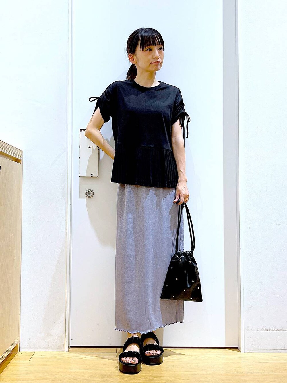 パープル系のスカート、ブラック系のショルダーバッグ、ブラック系のサンダルを着用したレディースの夏コーディネートの2枚目の写真