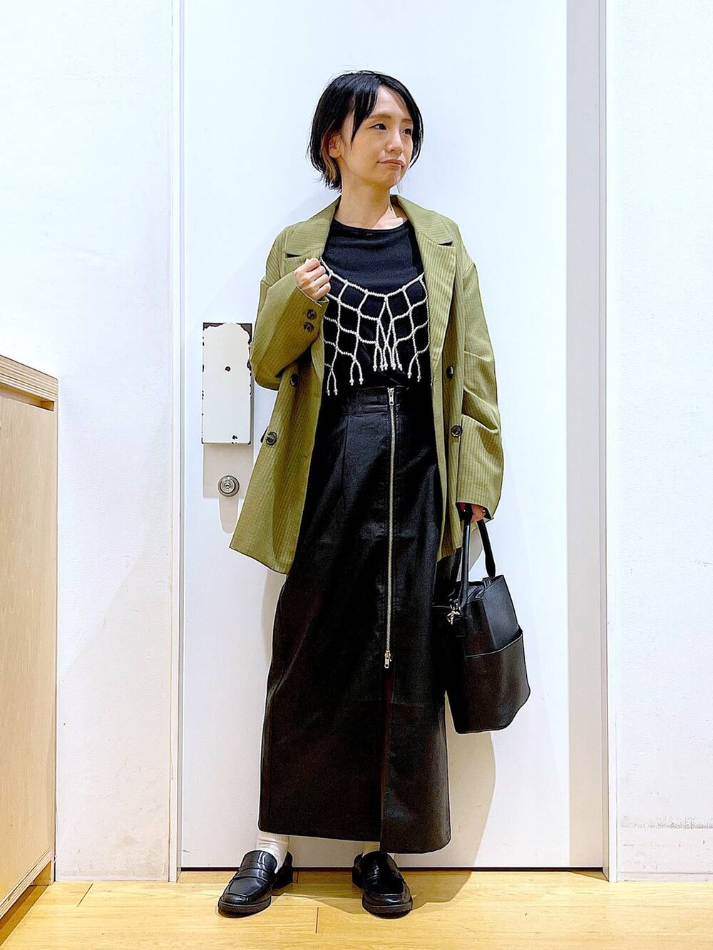 ホワイト系のベスト、ブラック系のスカート、ブラック系のショルダーバッグを着用したレディースの秋コーディネートの2枚目の写真