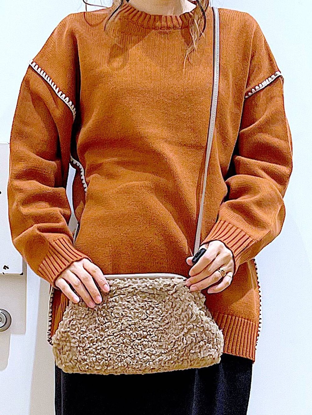 グレー系のスカート、オレンジ系のニット/セーター、ブラウン系のクラッチバッグを着用したレディースの冬コーディネートの9枚目の写真