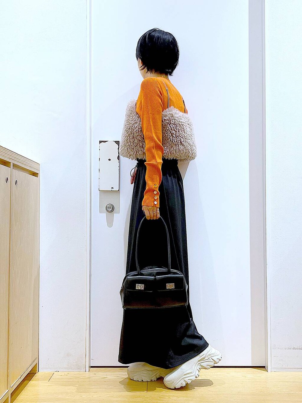 オレンジ系のニット/セーター、ブラウン系のベスト、ブラック系のハンドバッグを着用したレディースの秋コーディネートの3枚目の写真