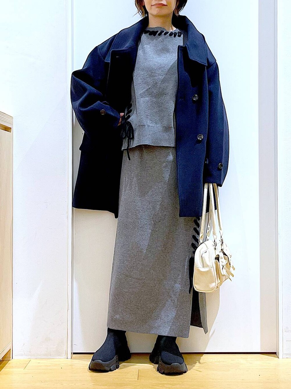 ブルー系のステンカラーコート、ホワイト系のハンドバッグ、ブラック系のブーツを着用したレディースの冬コーディネートの6枚目の写真